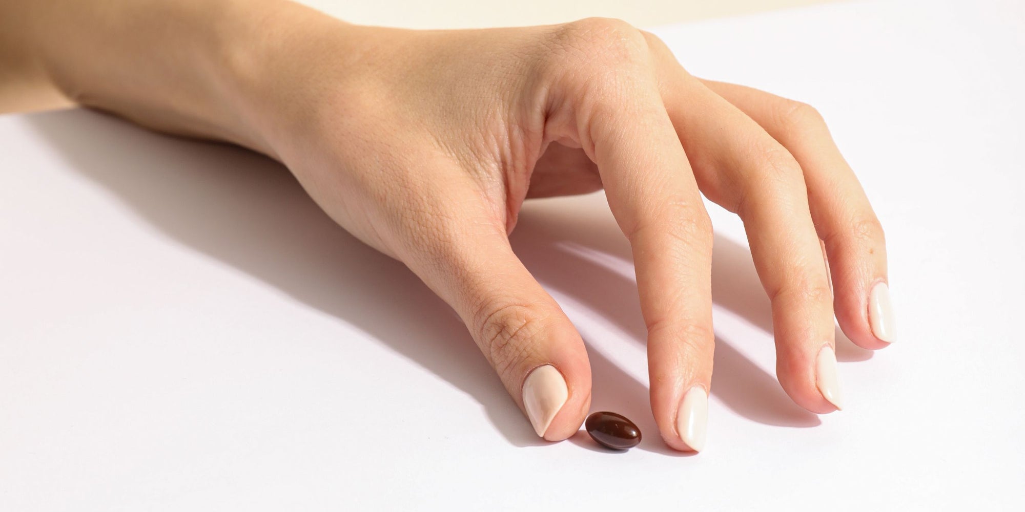 Mano de mujer con capsula marron en fondo blanco, complementos alimenticios de FARMA DORSCH nutricosmética