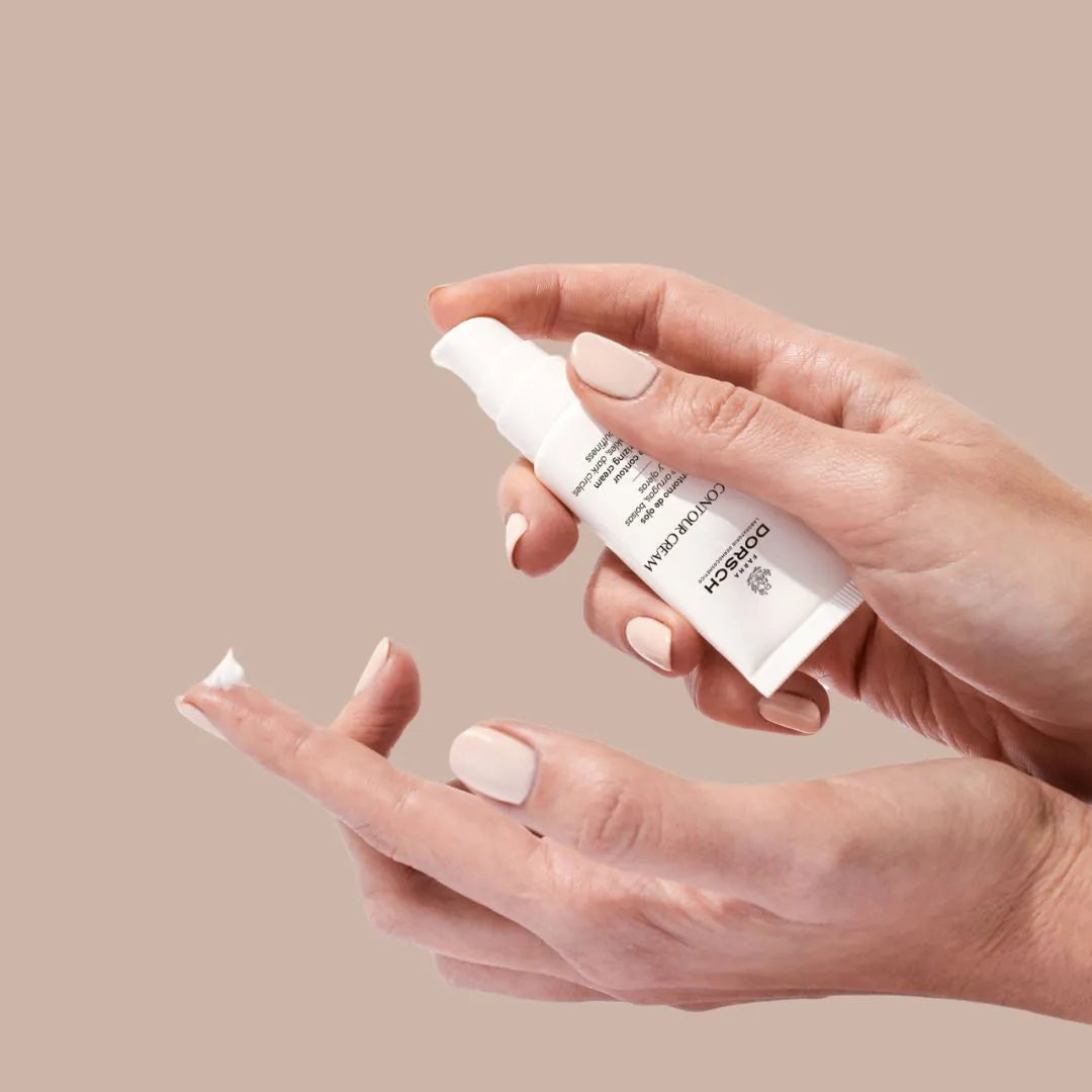 Manos aplicando la crema Eye Contour Cream de FARMA DORSCH sobre fondo neutro, tratamiento especifico para reducir bolsas, ojeras y arrugas, aportando hidratacion y firmeza al contorno ocular.