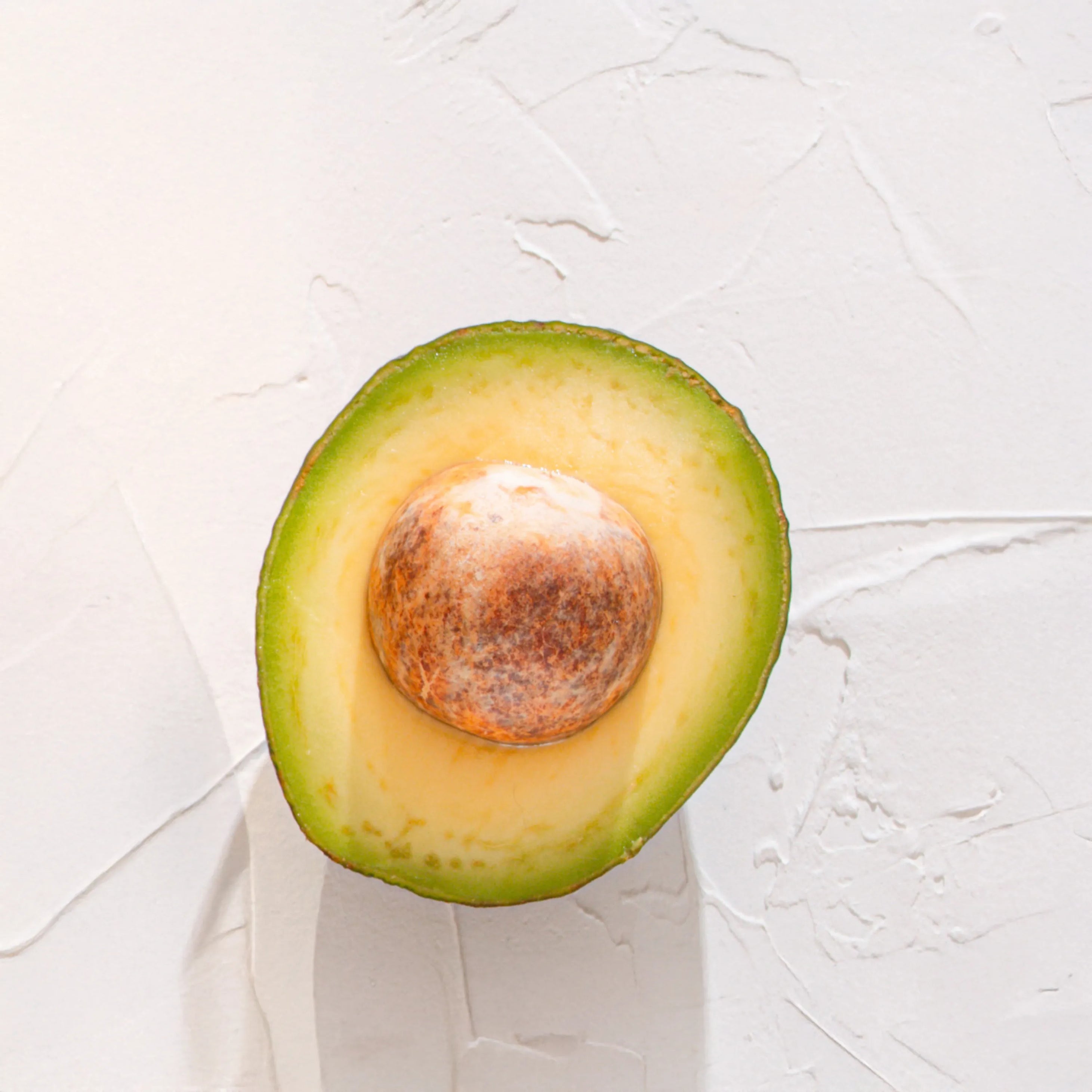 Medio aguacate con hueso representando Ingrediente activo Vitamina E Farma Dorsch con propiedades hidratantes, antioxidantes y nutritivas para tratamiento facial y corporal sobre fondo blanco suave en cosmetica natural española