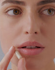 Primer plano de una mujer a punto de tomar un complemento alimenticio en cápsula, asociado a VISION BAGS & CIRCLES de FARMA DORSCH, formulado para combatir bolsas y ojeras desde el interior. Suplemento nutricosmético con ingredientes activos de alta eficacia.