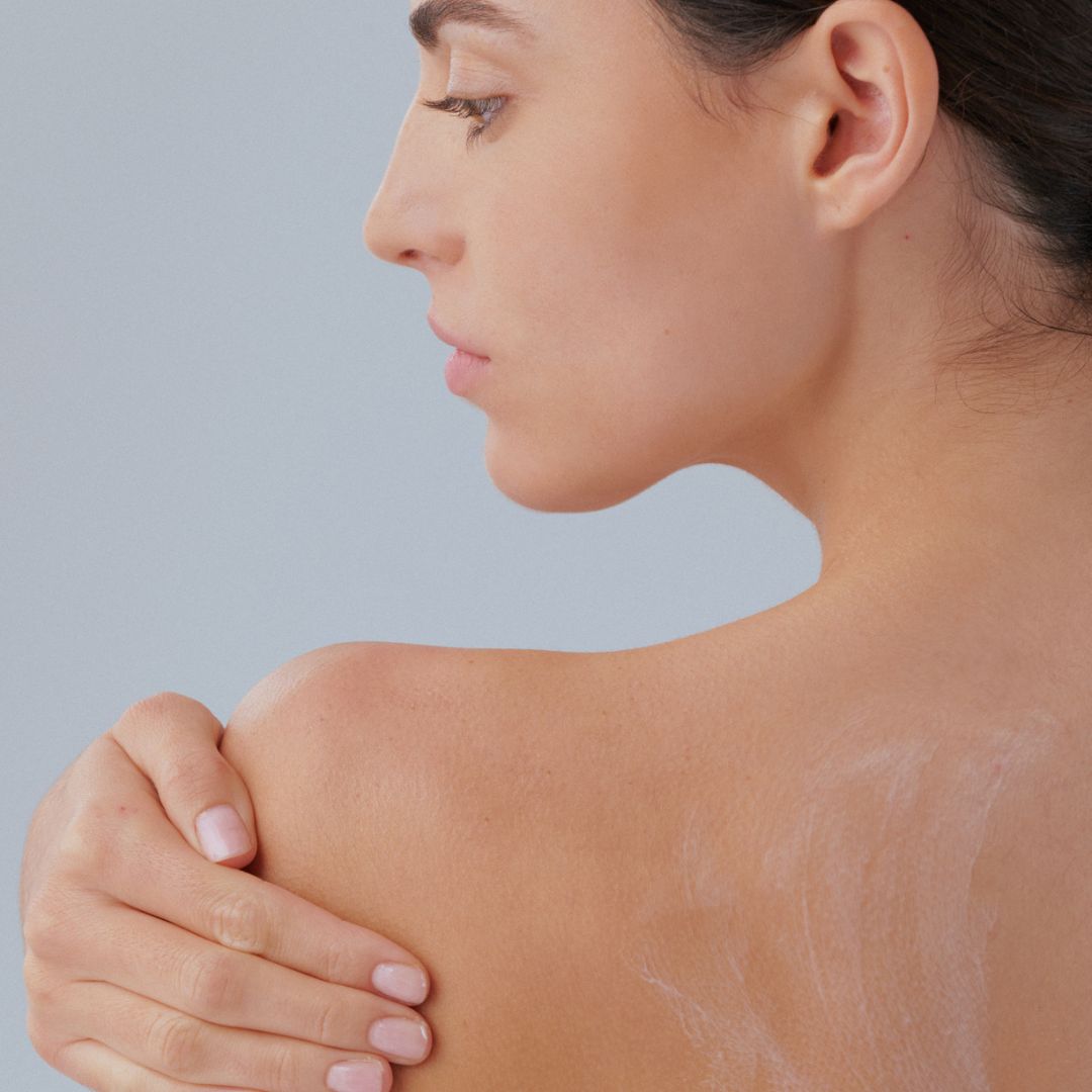 Mujer aplicando crema corporal hidratante FARMA DORSCH en fondo neutro gris