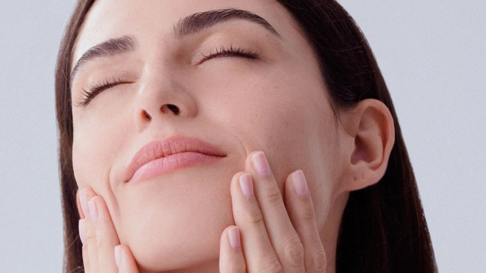 Mujer con el rostro iluminado y manos sobre las mejillas, representando la coleccion FARMA DORSCH para piel con manchas, diseñada para unificar el tono, reducir hiperpigmentaciones y mejorar la luminosidad cutanea.