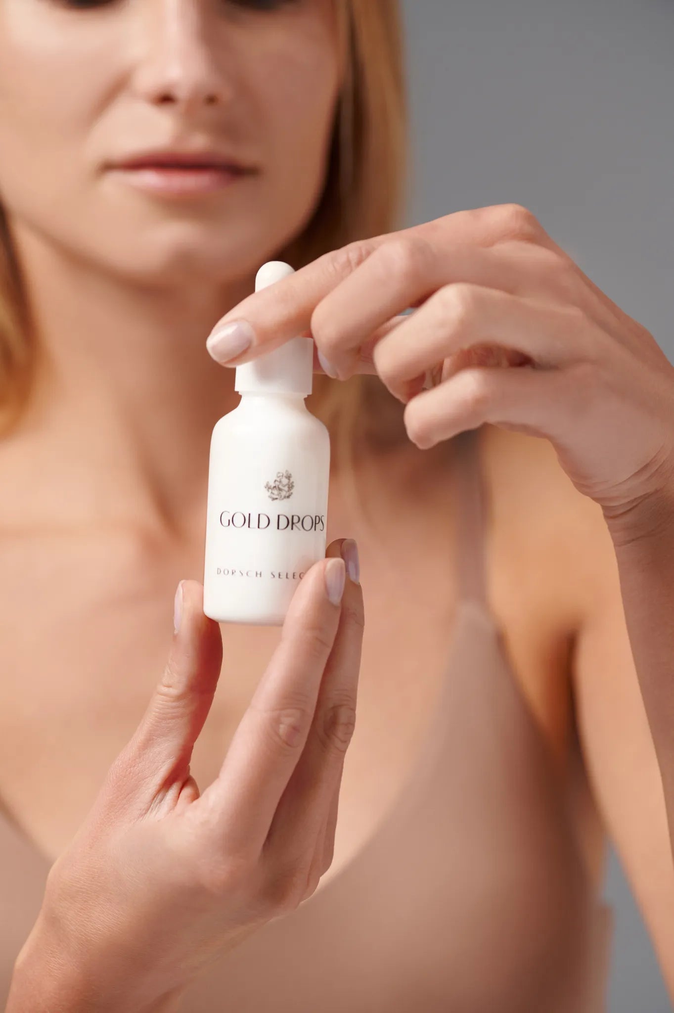 mujer abriendo y mostrando Gold Drops FARMA DORSCH aceite facial de tacto seco antiedad