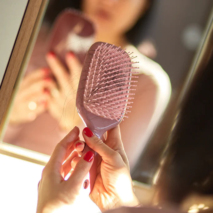 mujer sujetando un peine con cabello negro en él representando la cantidad de cabello que se le cae