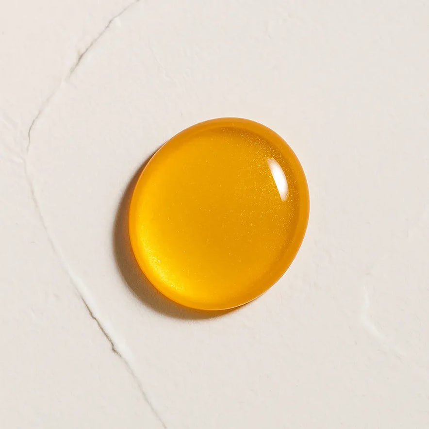 Gota amarilla de textura liquida brillante representando Ingrediente activo Coenzima Q10 Farma Dorsch para energía celular y protección antioxidante en tratamiento facial y corporal sobre fondo blanco marmolado en cosmética natural española