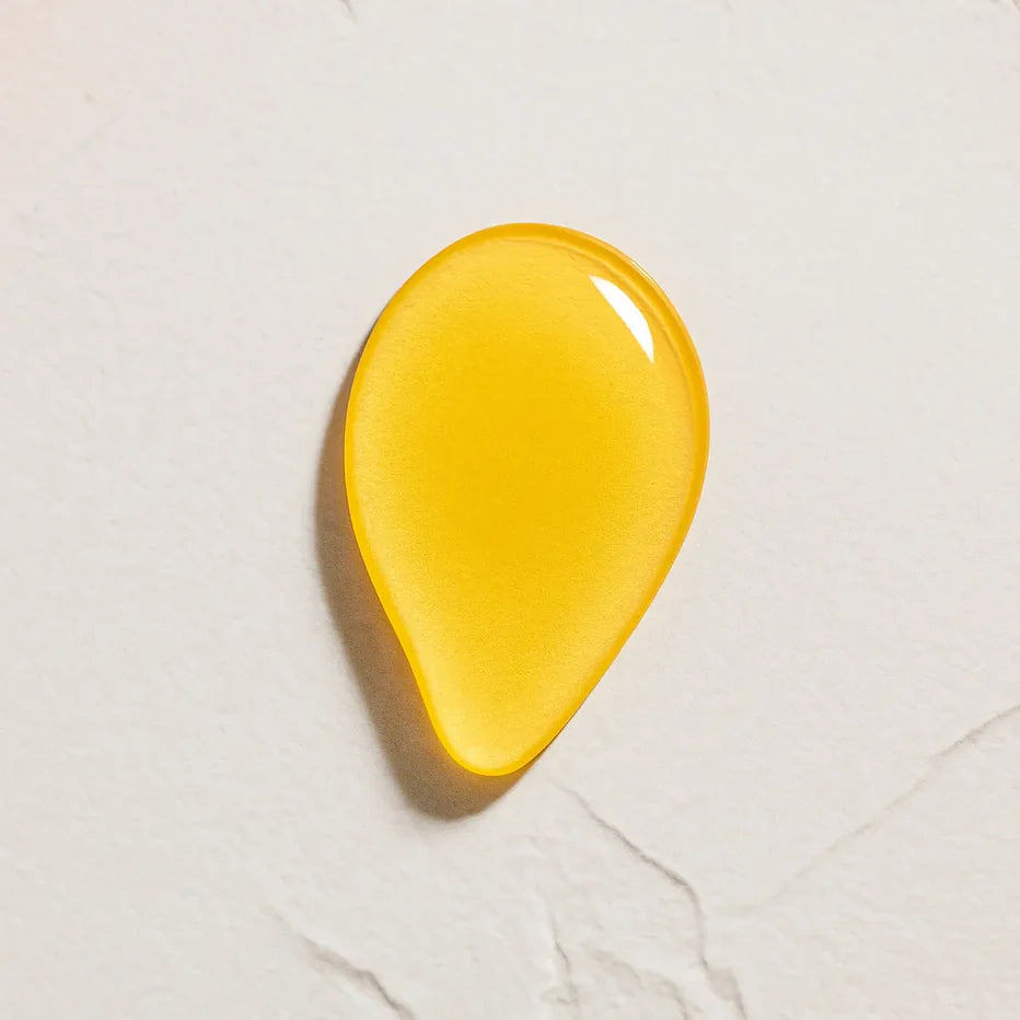 Gota amarilla de textura aceitosa brillante amarilla de Ingrediente activo Retinol Farma Dorsch para tratamiento antiedad y renovación de la piel sobre fondo blanco marmolado en cosmética natural española