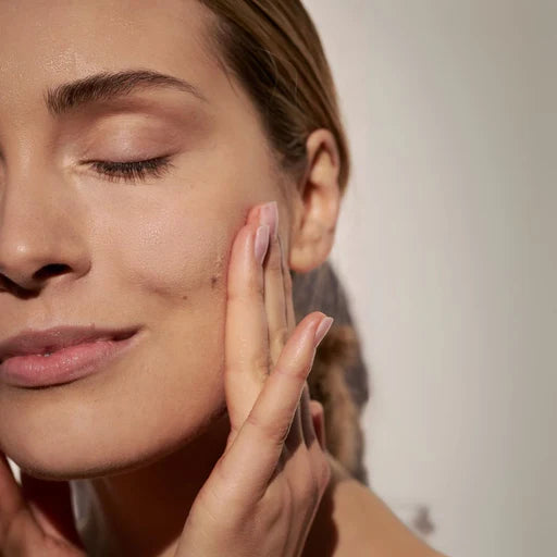 Mujer aplicando crema en rostro FARMA DORSCH dermocosmectica en fondo neutro gris 