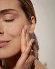 Mujer aplicando crema en rostro FARMA DORSCH dermocosmectica en fondo neutro gris 