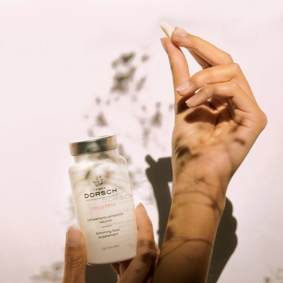 Persona sosteniendo una cápsula y el envase del complemento alimenticio Slim &amp; Firm de Farma Dorsch, ilustrando su modo de uso.