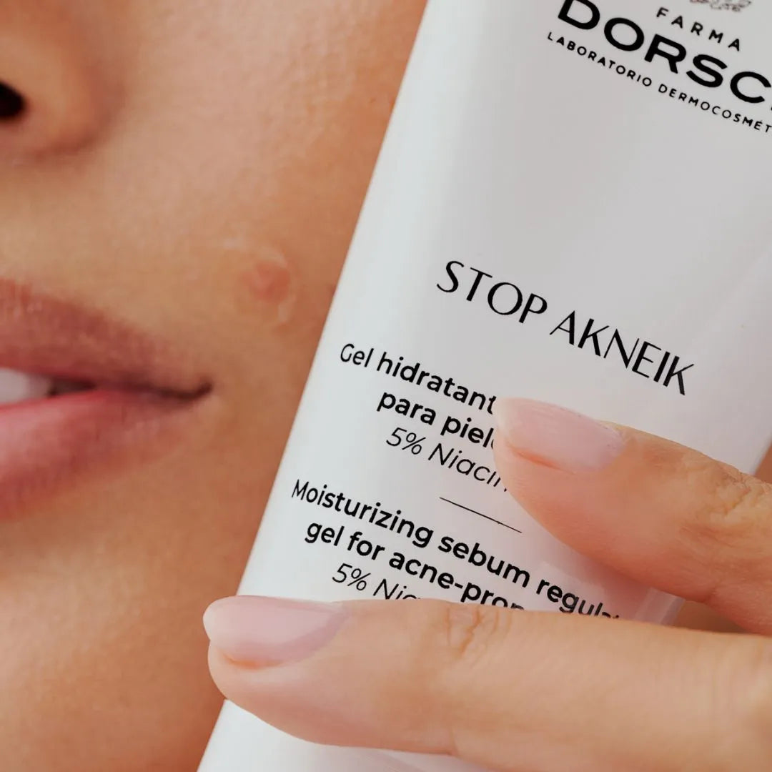 Primer plano de un rostro con imperfecciones aceneicas visibles sujetando el gel hidratante STOP AKNEIK de FARMA DORSCH. Tratamiento con 5% de niacinamida, formulado para pieles acneicas. Hidrata, regula el sebo y ayuda a reducir marcas y brotes de acné. taratmiento para la piel con tendencia acenéica